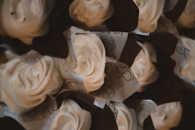 Creamy, swirled icing adorns cupcakes, each wrapped with decorative brown and white paper. The arrangement is tightly packed, highlighting the intricate designs and texture of the frosting.