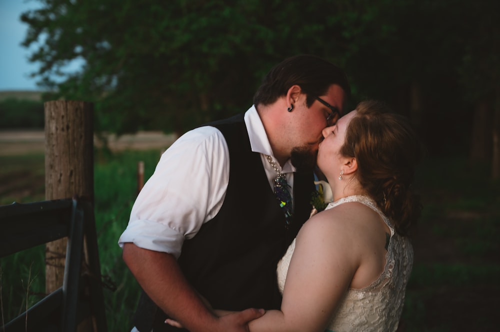 a bride and groom kissing in front of a fence