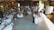 A rustic venue is decorated for a wedding reception featuring round tables with white tablecloths, floral centerpieces, and guests seated around them. A couple is dancing in the center under soft lighting. String lights and draped fabric add to the cozy atmosphere. On the sides, people are observing the dance, and there's a vintage ambiance with wooden walls and soft green accents.
