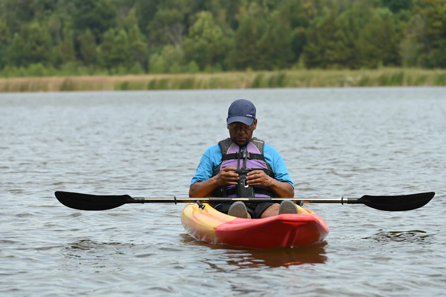 Man sitting in a kayak on a river checking his phone while paddling