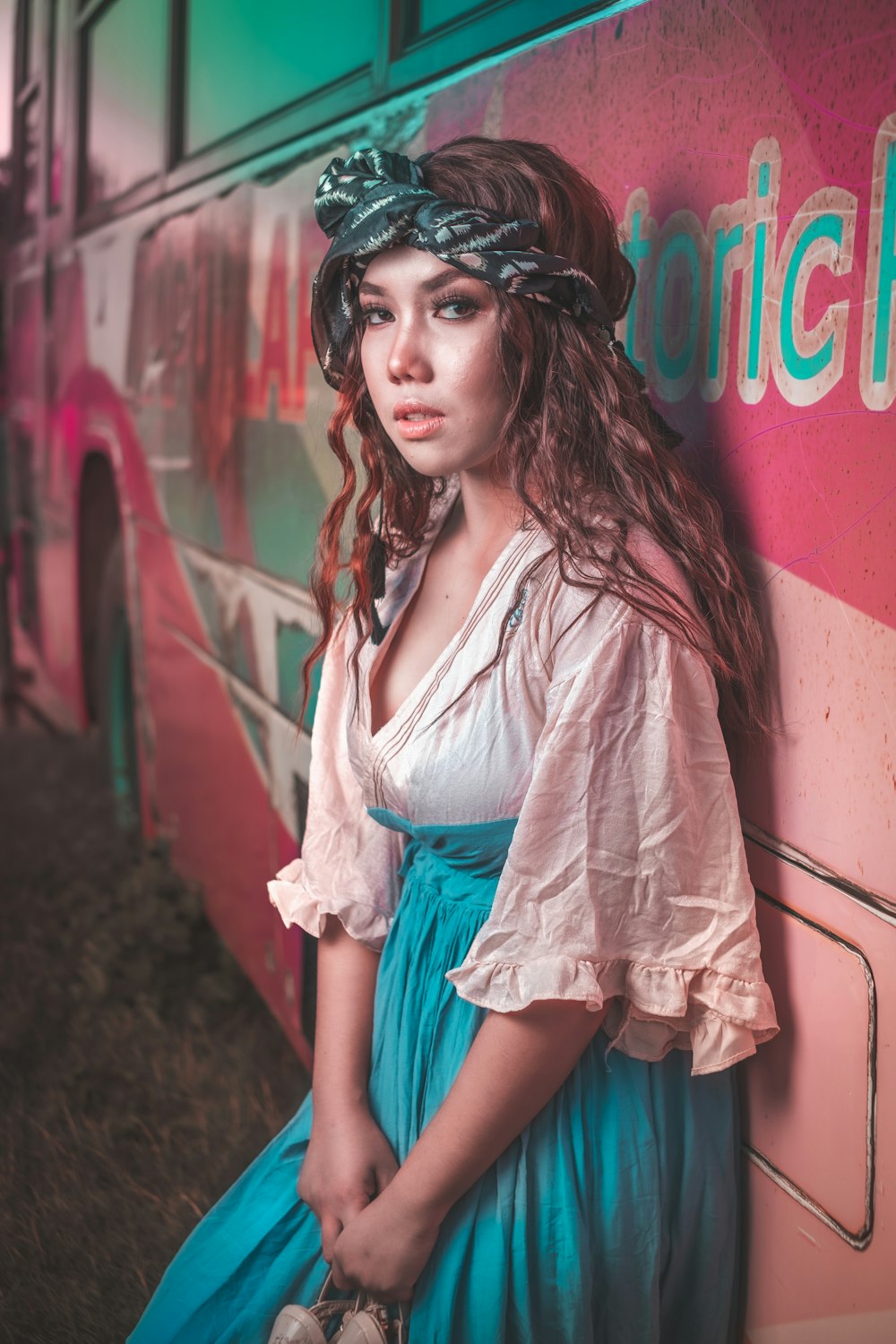 a woman in a blue dress leaning against a bus