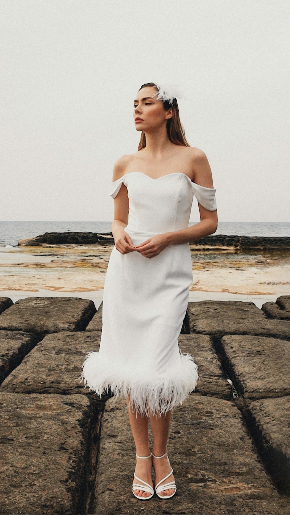 a woman in a white dress standing on a rocky beach