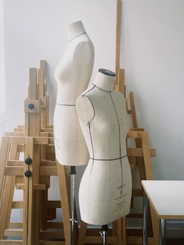 A sleek, minimalistic studio setting with a stylist adjusting a dark, elegant garment on a mannequin.