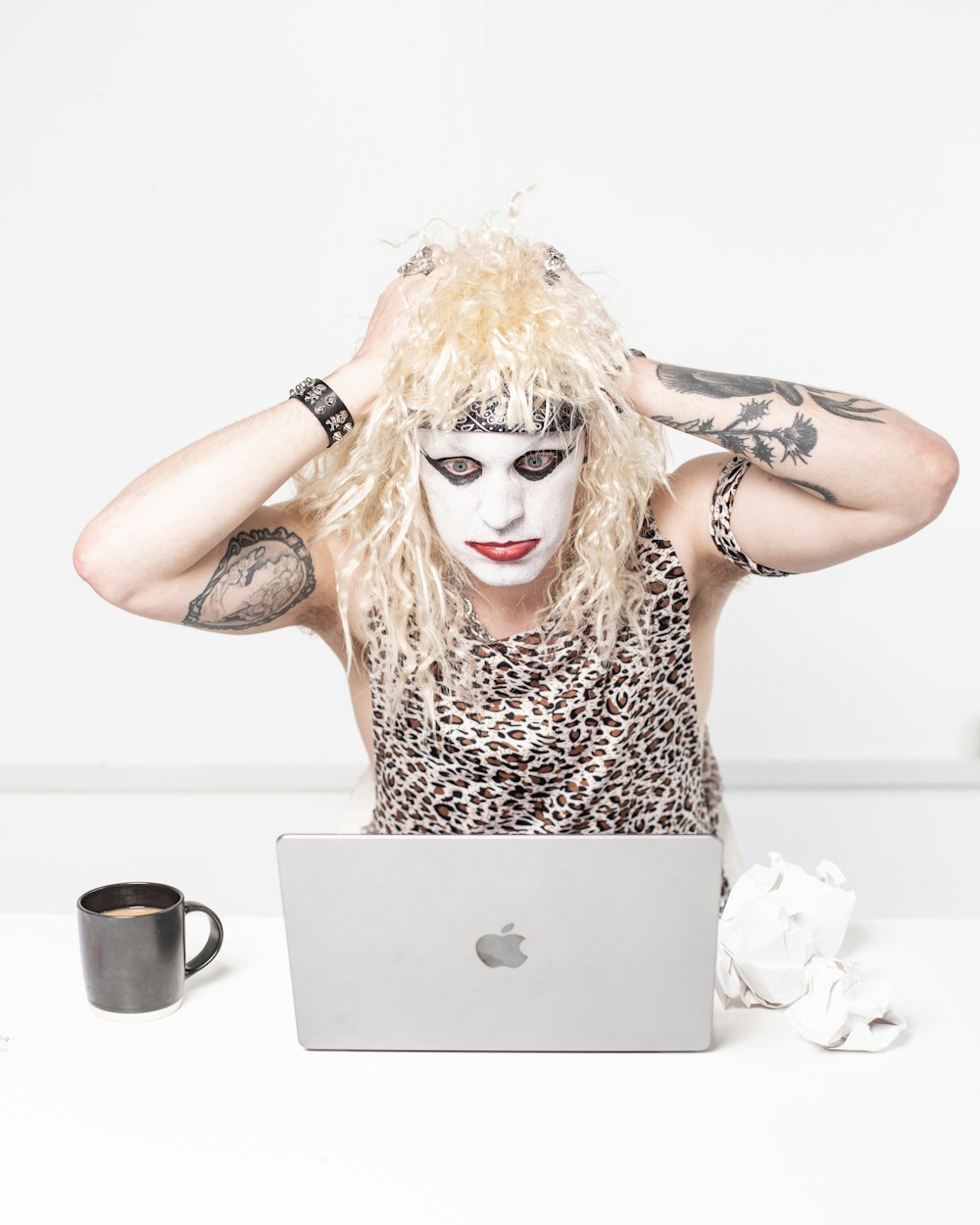 a man with white makeup and makeup on his face sitting in front of a laptop