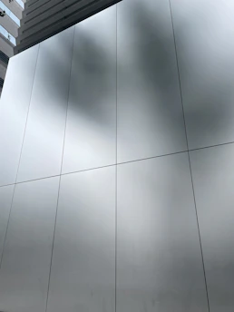 Close-up of sleek aluminum facade panels reflecting a modern city skyline under a clear sky.
