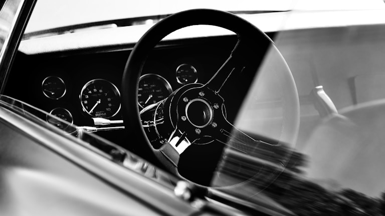Black and white close-up of a vintage car tachometer glowing softly.