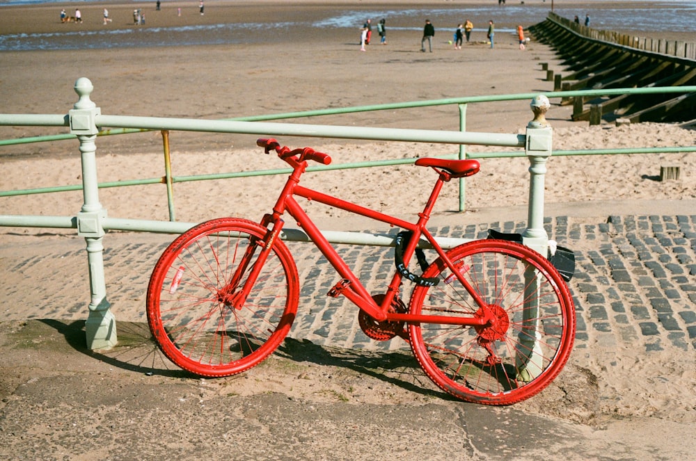 a red bicycle parked on a beach next to a fence