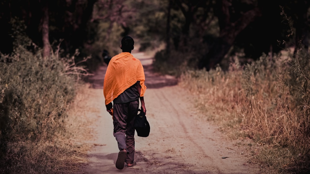 Un hombre caminando por un camino de tierra cargando una bolsa