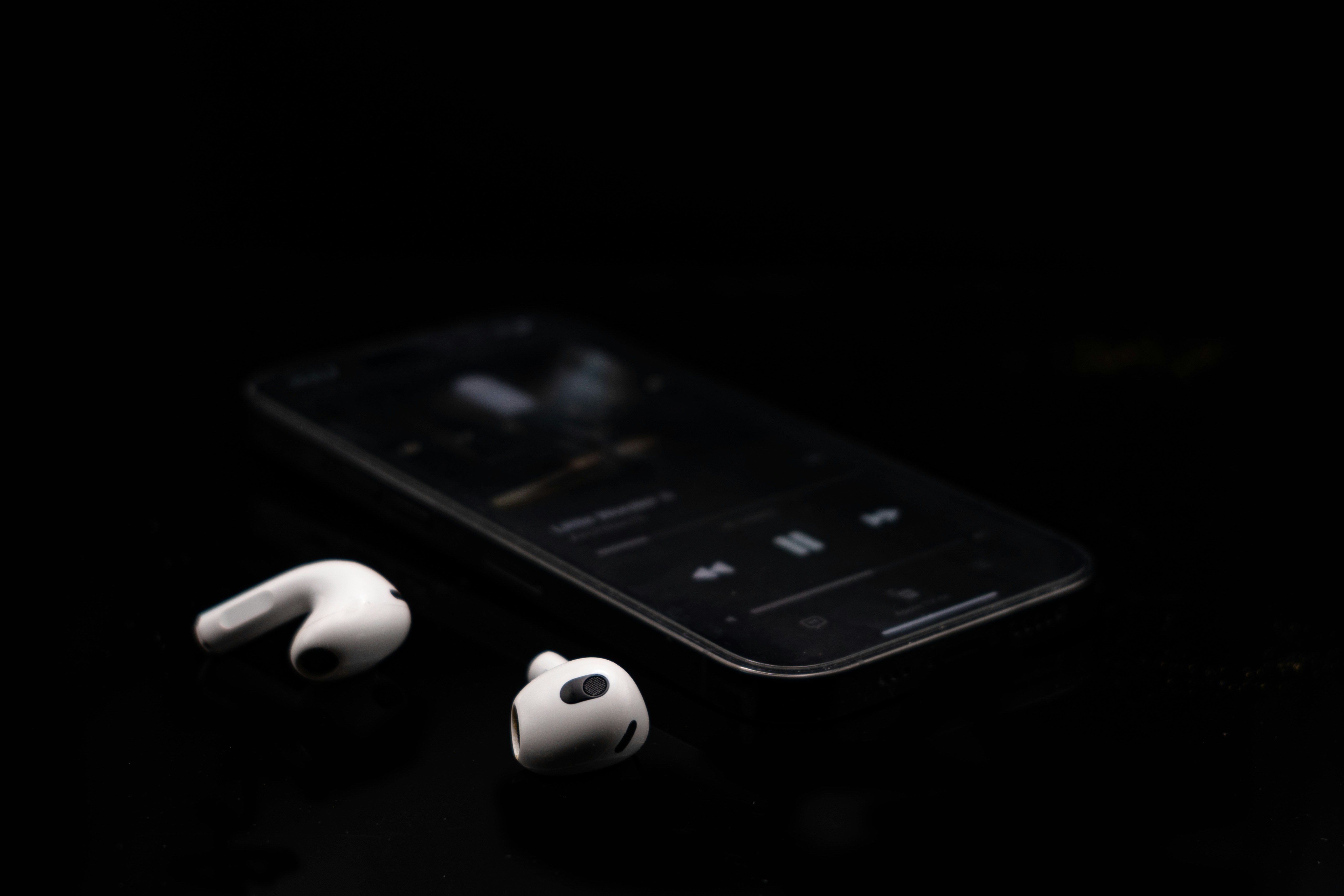 A pair of white Apple AirPods sit in their open charging case, with a phone screen displaying a graphical equalizer interface in the background.