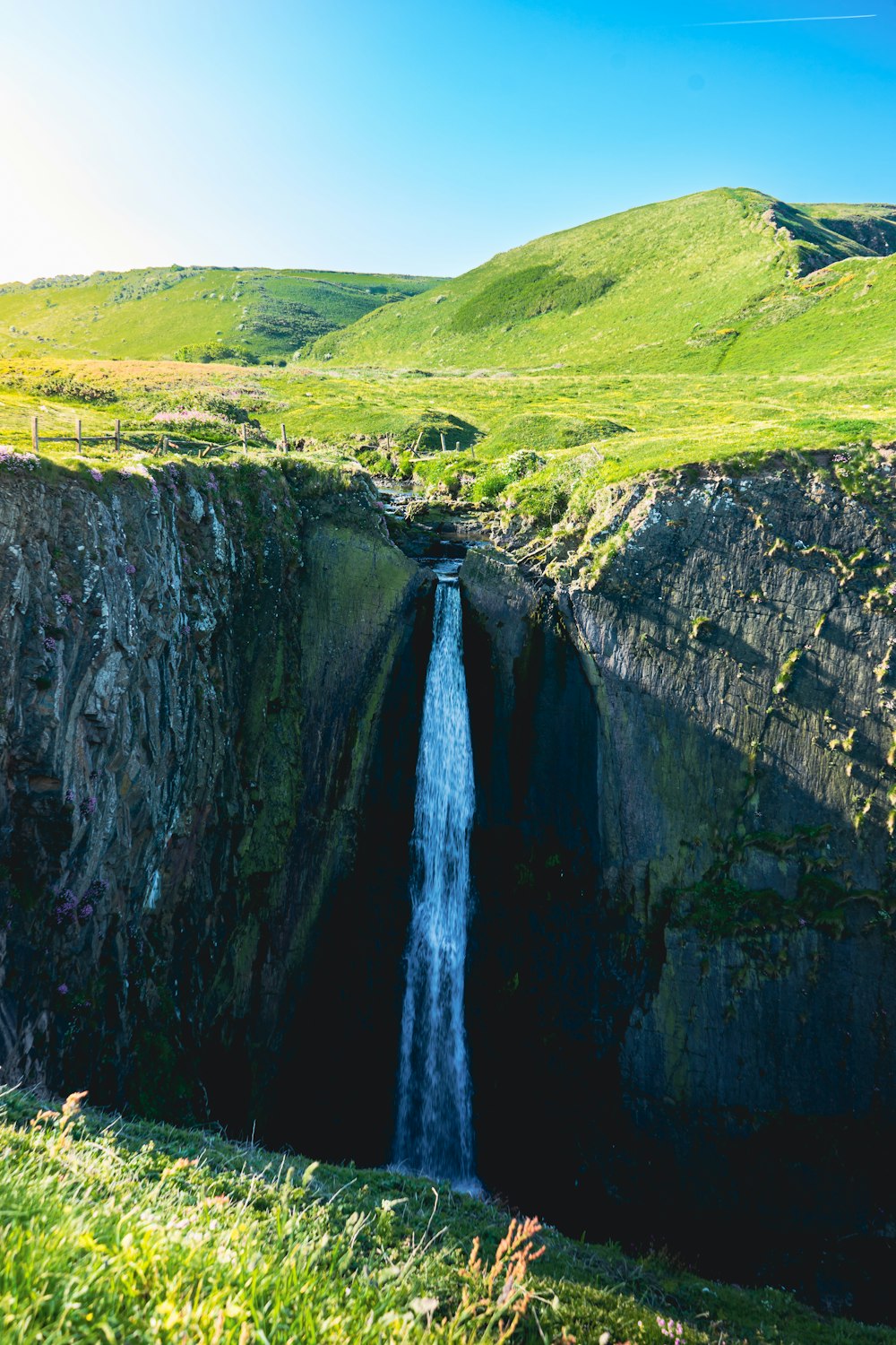 a small waterfall in the middle of a green valley