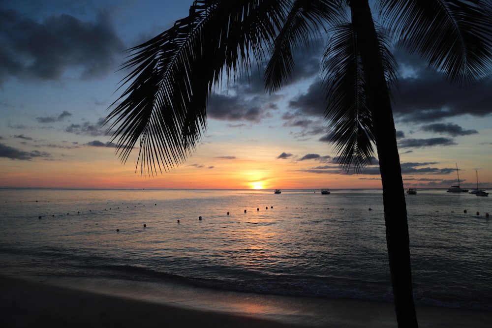 the sun is setting over the ocean with boats in the water