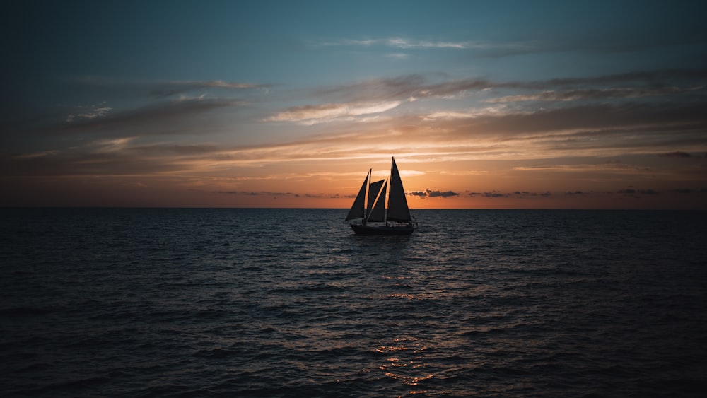 a sailboat in the middle of the ocean at sunset