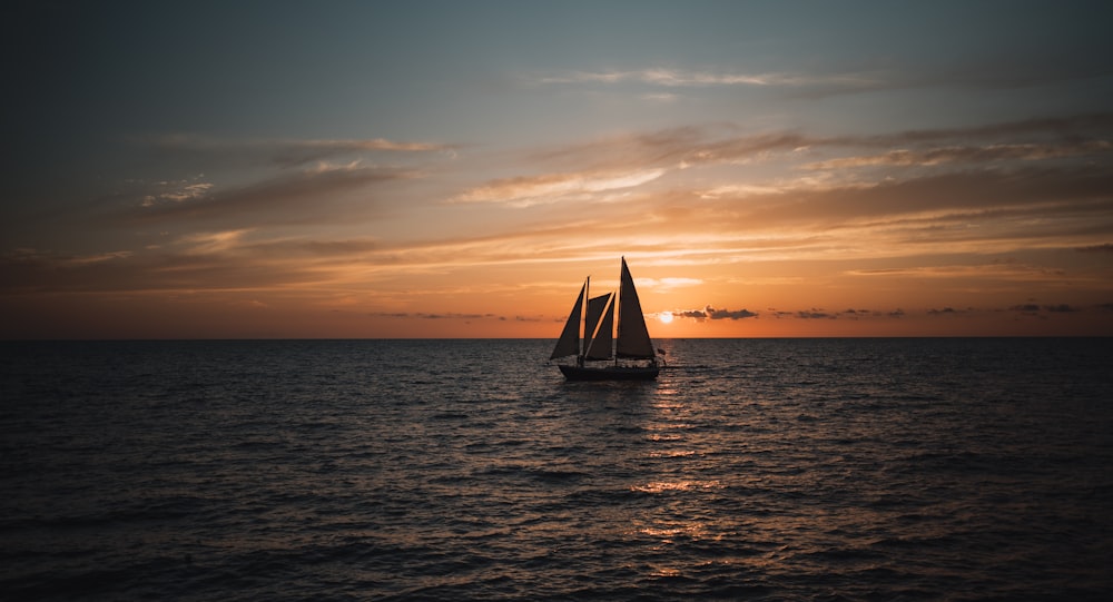 a sailboat in the middle of the ocean at sunset