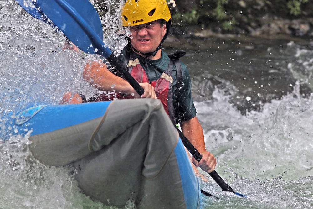 a man in a yellow helmet is paddling a blue kayak