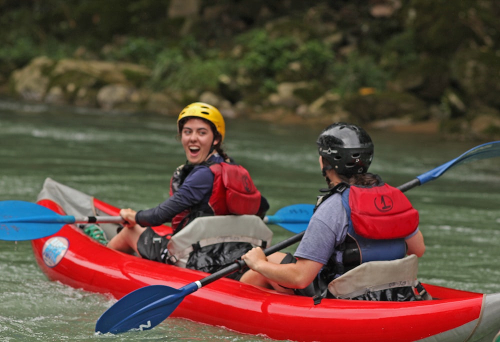 a couple of people riding on top of a red kayak