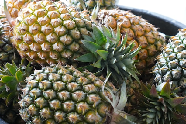 Several pineapples piled together with varying shades of green and ripe yellow, featuring textured skin and prominent leaves.