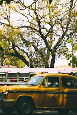A vibrant yellow cab cruising through Dehradun city streets lined with trees and shops
