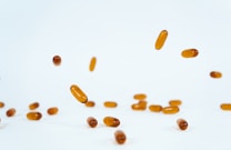 Several brown capsules are scattered and suspended against a plain white background, giving a sense of motion and lightness.