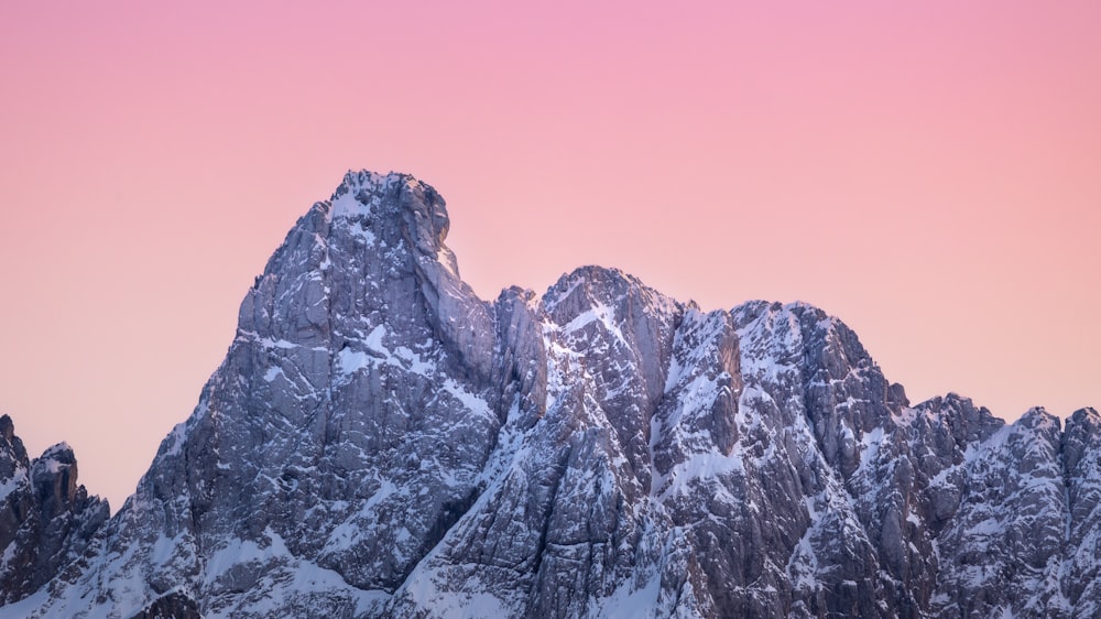 a mountain range covered in snow under a pink sky