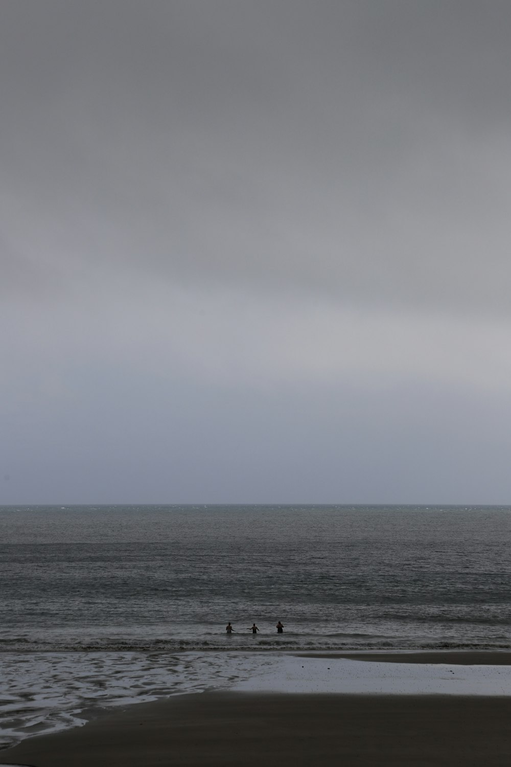 a couple of people walking along a beach under a cloudy sky