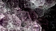 Clusters of translucent amethyst crystals with distinct geometric facets bathed in low light, creating an intricate play of reflections and shadows.