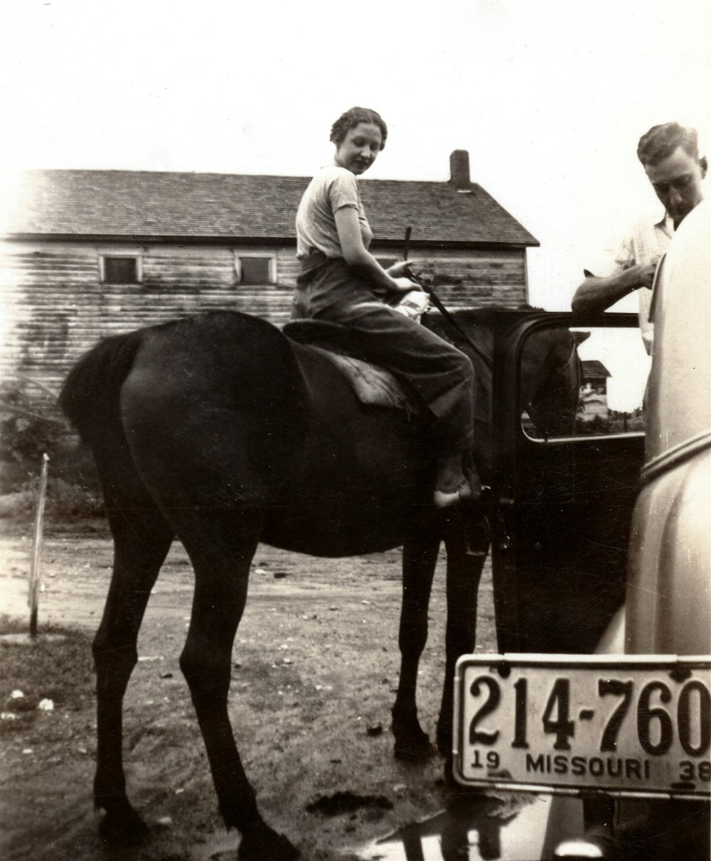 a woman sitting on top of a horse next to a car