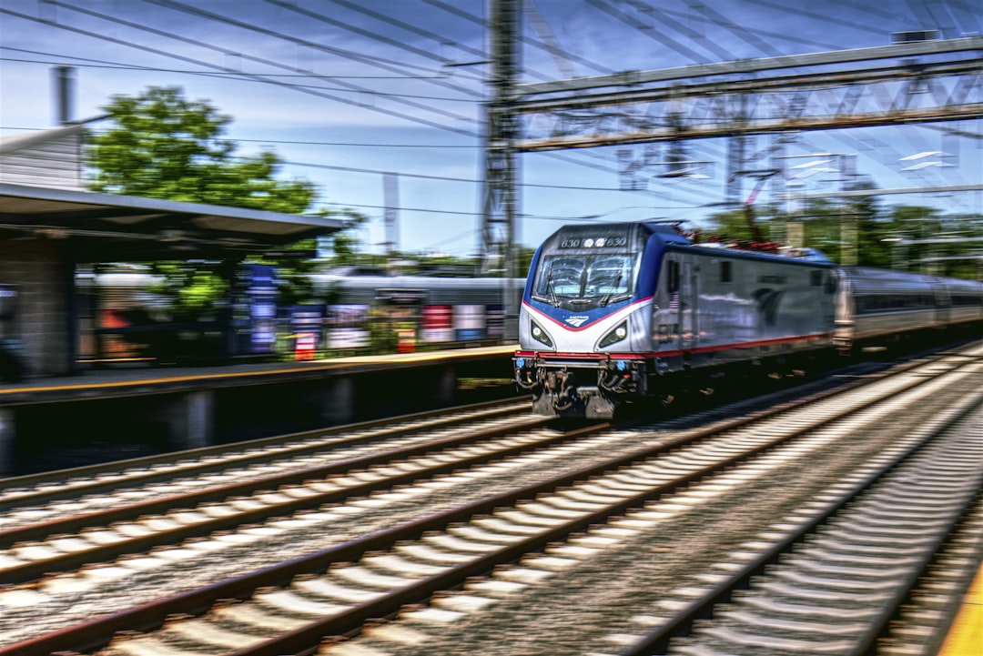 a train traveling down train tracks next to a station, An Amtrak ACS64 flies by Princeton Junction.