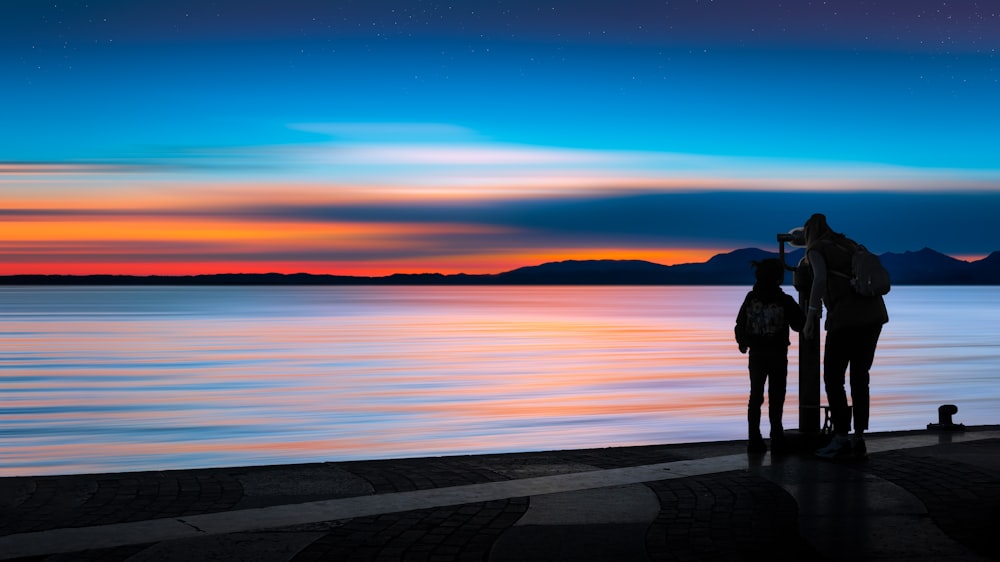 a couple of people standing next to a body of water