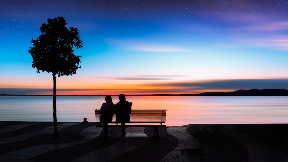 two people sitting on a [UNK] near a body of water