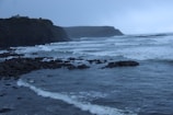 Waves crashing against rocky cliffs under a cloudy sky.