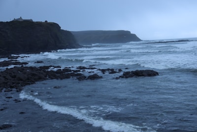 Waves crashing against rocky cliffs under a cloudy sky.