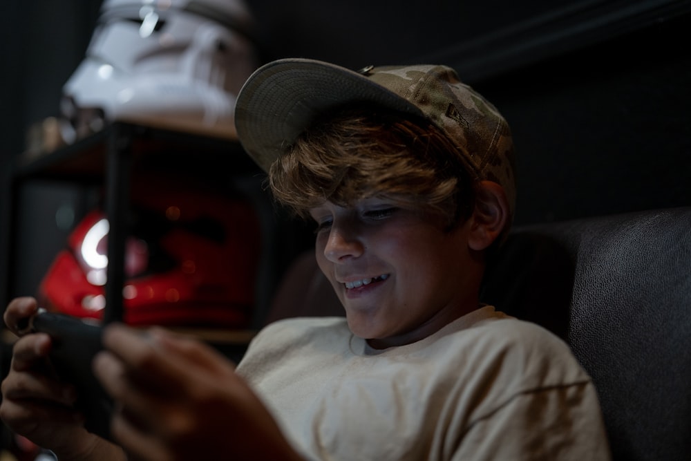 a young boy sitting in a chair looking at a cell phone