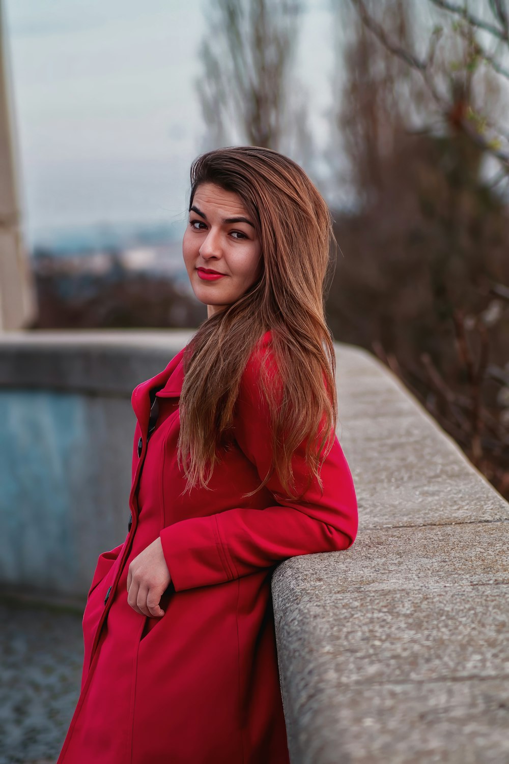 a woman in a red coat leaning against a wall