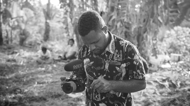 A creator using a portable microphone and headphones while recording audio in a forest setting