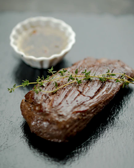 Close-up of a sizzling gourmet steak plated with fresh herbs and a drizzle of sauce.
