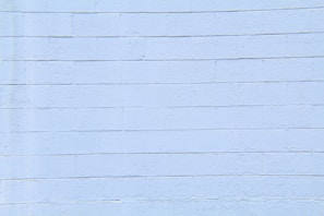A light blue concrete block wall with visible horizontal and vertical seams. The surface appears smooth with slight textures and imperfections.