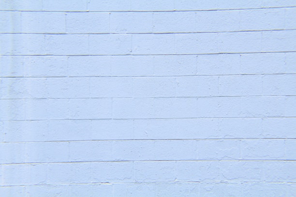 A light blue concrete block wall with visible horizontal and vertical seams. The surface appears smooth with slight textures and imperfections.