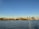 A city skyline with modern skyscrapers and the prominent Space Needle against a clear blue sky. The view is from across a body of water with gentle ripples reflecting the sunlight.
