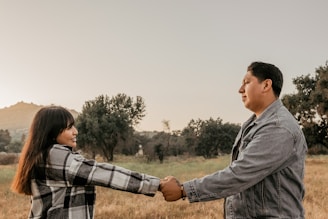 A couple holding hands, smiling warmly in a peaceful outdoor setting.