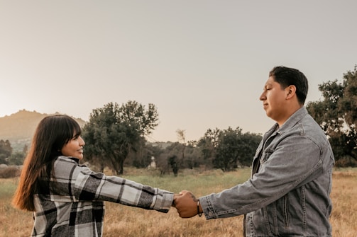 A couple holding hands, smiling warmly in a peaceful outdoor setting.