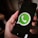 A close-up image of a hand holding a smartphone with the WhatsApp logo displayed prominently on the screen. The logo is green and white, centered against a black background.
