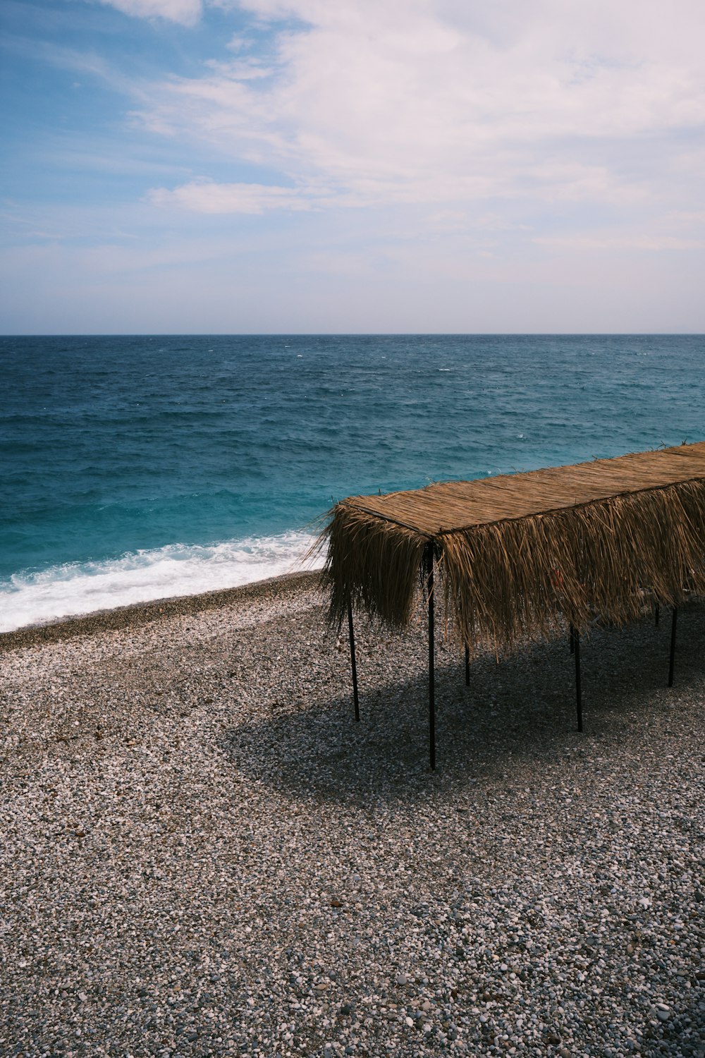 a thatch covered bench on a rocky beach