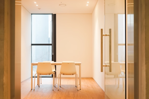 Minimalist conference room with natural light highlighting a polished wooden table and leather chairs.