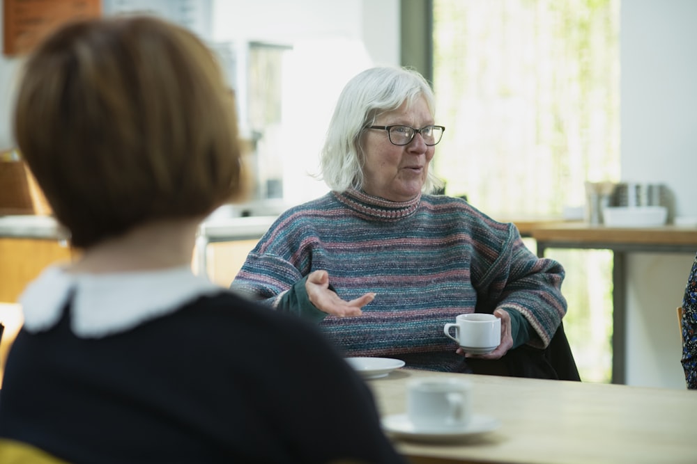 a woman sitting at a table talking to another woman