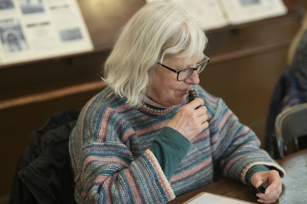 a woman sitting at a table with a pen in her mouth