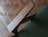 A close-up of a wooden chair armrest set against a green fabric, with a blurred wooden parquet floor in the background.