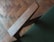 A close-up of a wooden chair armrest set against a green fabric, with a blurred wooden parquet floor in the background.