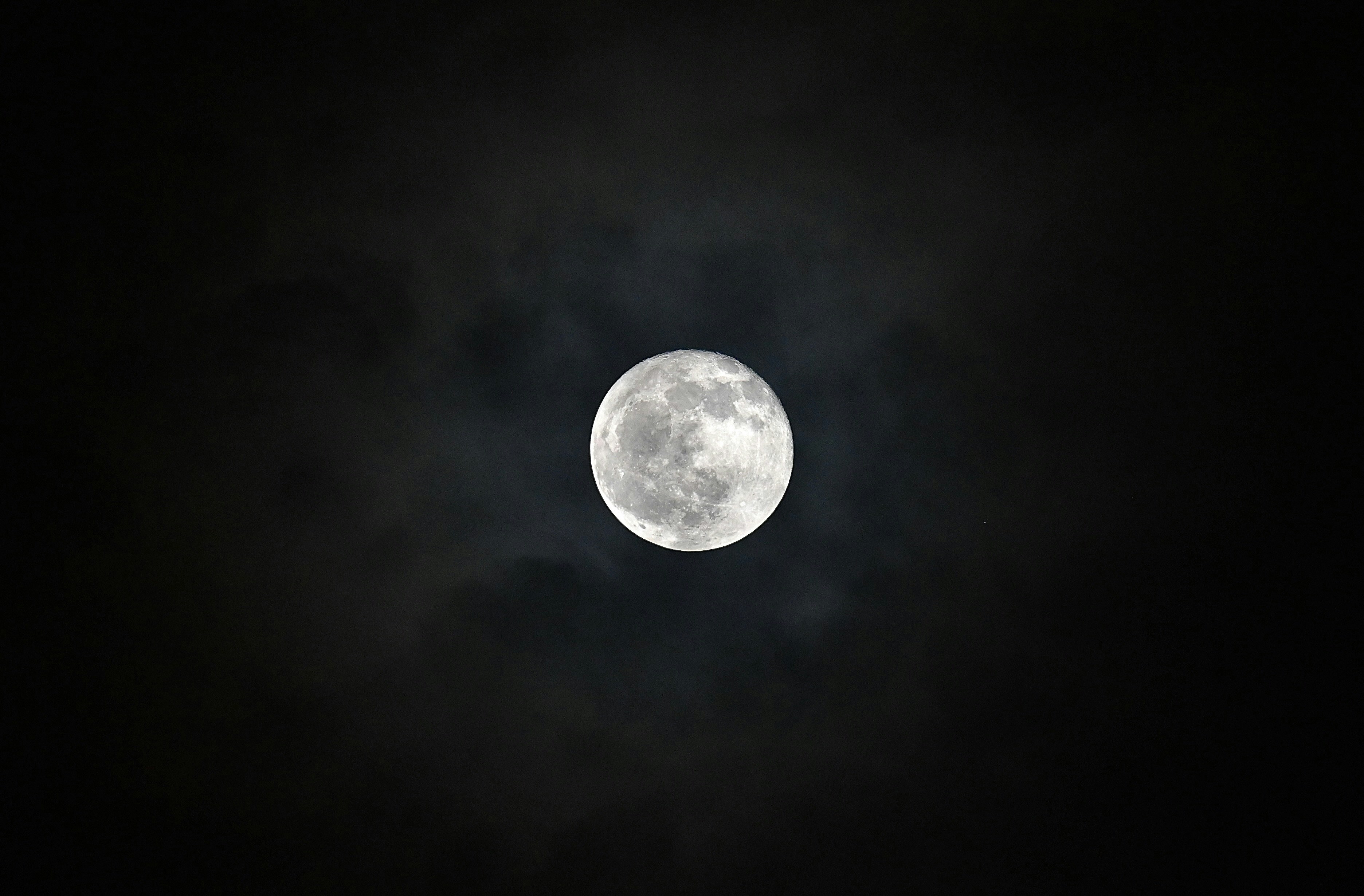 a full moon in the dark sky with clouds