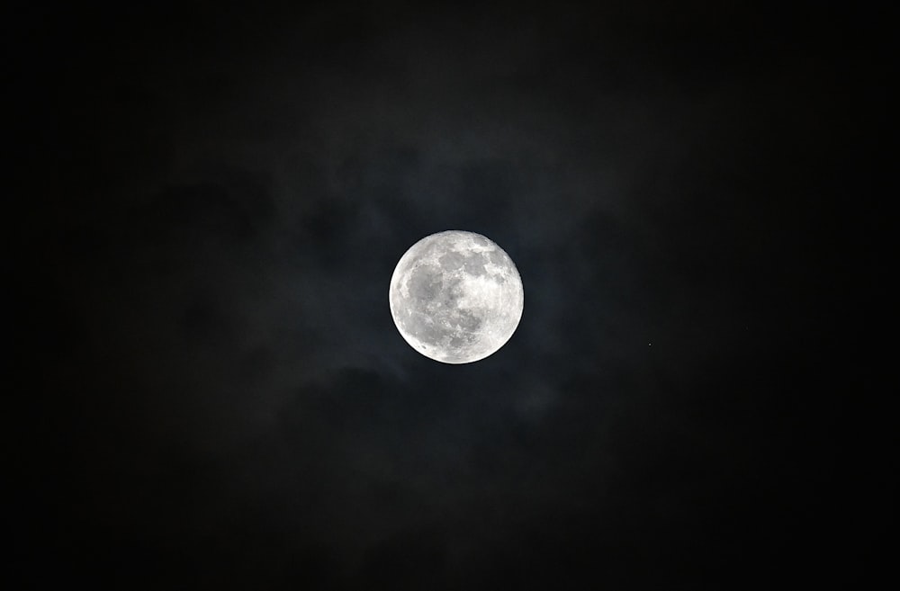 a full moon in the dark sky with clouds