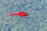 A helicopter hovering over a green forest landscape.